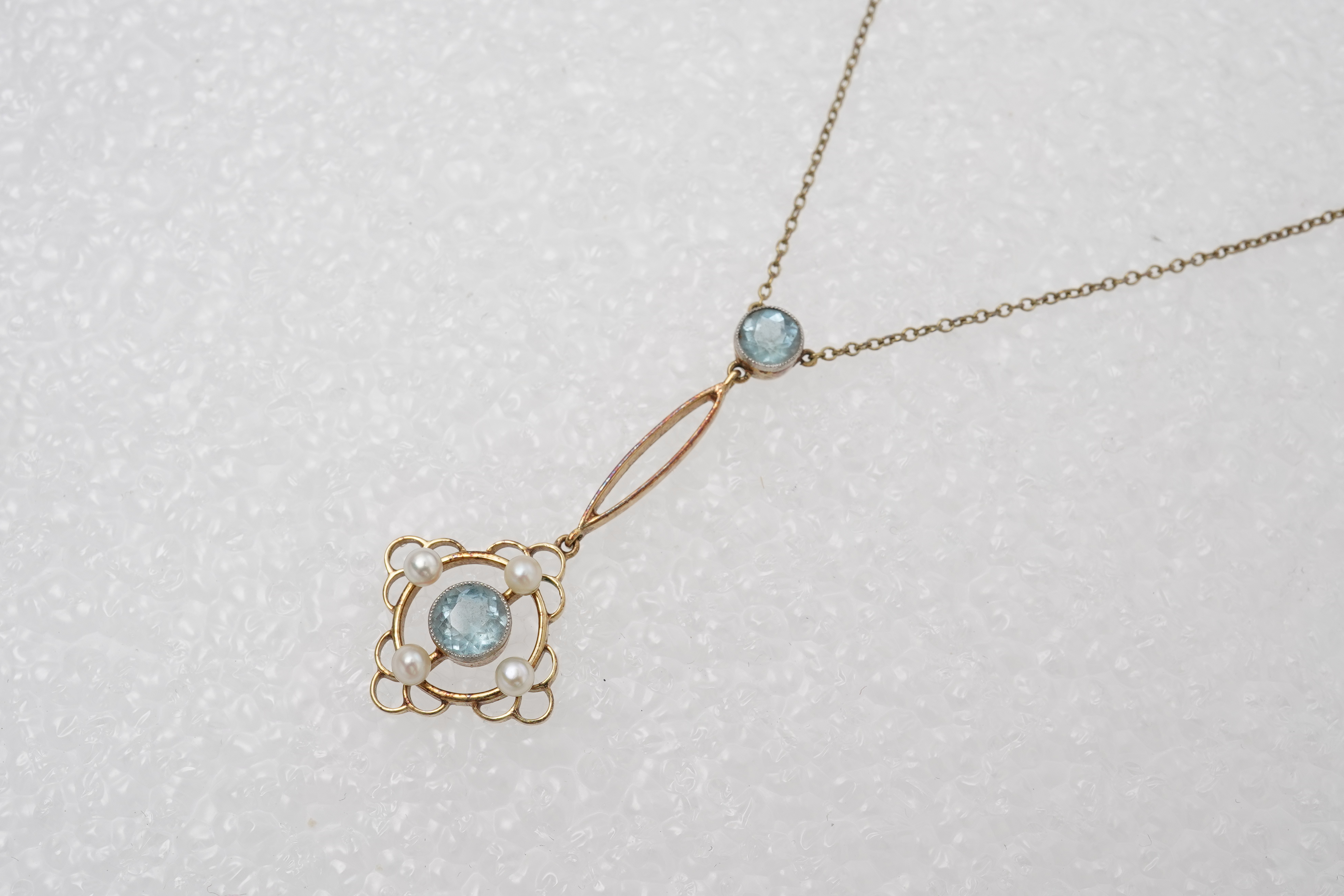 An Edwardian circular-cut aquamarine and seed pearl pendant, early 20th century, of foliate design, mounted in gold, pendant length 4cm, chain length 40cm, clasp stamped 15, gross weight approximately 3 grams, pearls unt